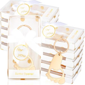 May include: Gold-colored bottle opener in the shape of a foot, packaged in a clear box with a white ribbon and a "for you" sticker. The box is inside a white box with gold polka dots. The words "Bottle Opener" are printed on the box.