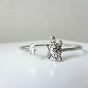 May include: Silver bracelet with a penguin and a turtle charm. The bracelet is made of twisted wire.