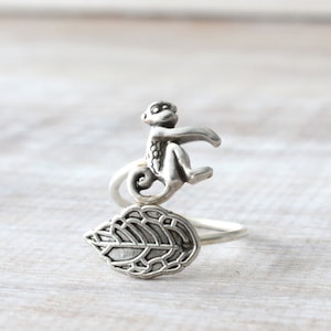 Könnte beinhalten: Ein silberner Ring mit einer Affenfigur, die auf einem Blattdesign sitzt.