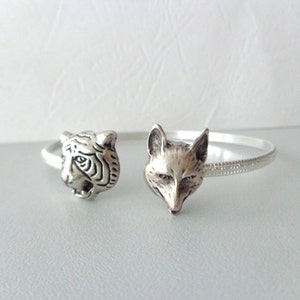 May include: Silver bracelet with a tiger and fox head design. The bracelet is thin and has a textured surface.
