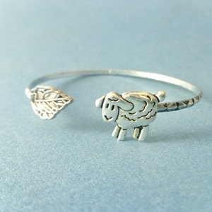 Pode incluir: Um bracelete de prata com um design de folha em uma extremidade e um design de ovelha na outra.