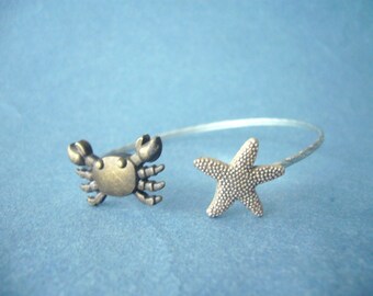 May include: A silver bangle bracelet with a gold crab and a silver starfish charm. The bracelet is on a blue background.