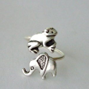 Puede incluir: Un anillo de plata con una rana sentada encima de un elefante. El anillo es ajustable y se puede llevar en cualquier dedo.