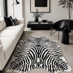 Puede incluir: Una alfombra grande de forma irregular con un patrón de rayas de cebra en blanco y negro de alto contraste. La alfombra tiene una silueta natural y orgánica con bordes curvos, imitando la apariencia de una piel, colocada sobre el suelo.