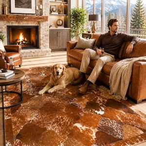 Puede incluir: Salón con sofá de cuero marrón, un golden retriever y una alfombra de piel de vaca. La alfombra tiene parches marrones y blancos. Una chimenea y vistas a la montaña son visibles a través de la ventana.