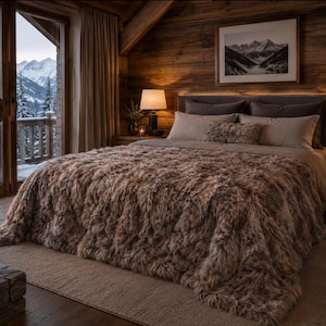 Puede incluir: Un dormitorio acogedor con una cama grande cubierta con una manta marrón y peluda. La habitación tiene paredes de madera y una vista de montañas cubiertas de nieve a través de una gran ventana. Dos lámparas están en las mesitas de noche.