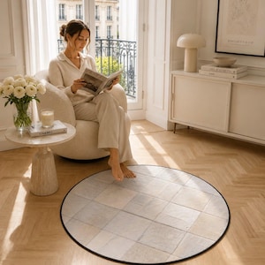 Peut inclure: Un tapis rond avec un motif géométrique de carrés beiges clairs et gris, bordé d'une bordure noire. Le tapis est posé sur un parquet, créant un élément de design intérieur confortable et élégant.