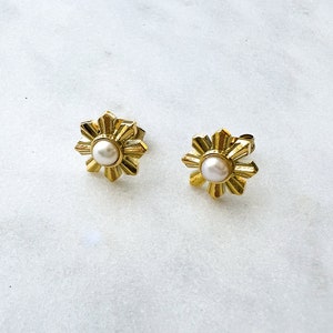 May include: A pair of gold-tone earrings with a pearl in the center of each earring. The earrings are shaped like a flower with multiple points.