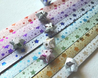 May include: An assortment of colorful paper strips with star patterns and origami stars. The strips are in various colors, including pink, purple, blue, and gold, with metallic finishes. The origami stars are silver.