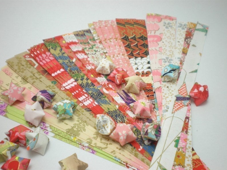 May include: A collection of colorful origami stars made from patterned paper strips. The strips are arranged in a fan shape, with the stars scattered around them.