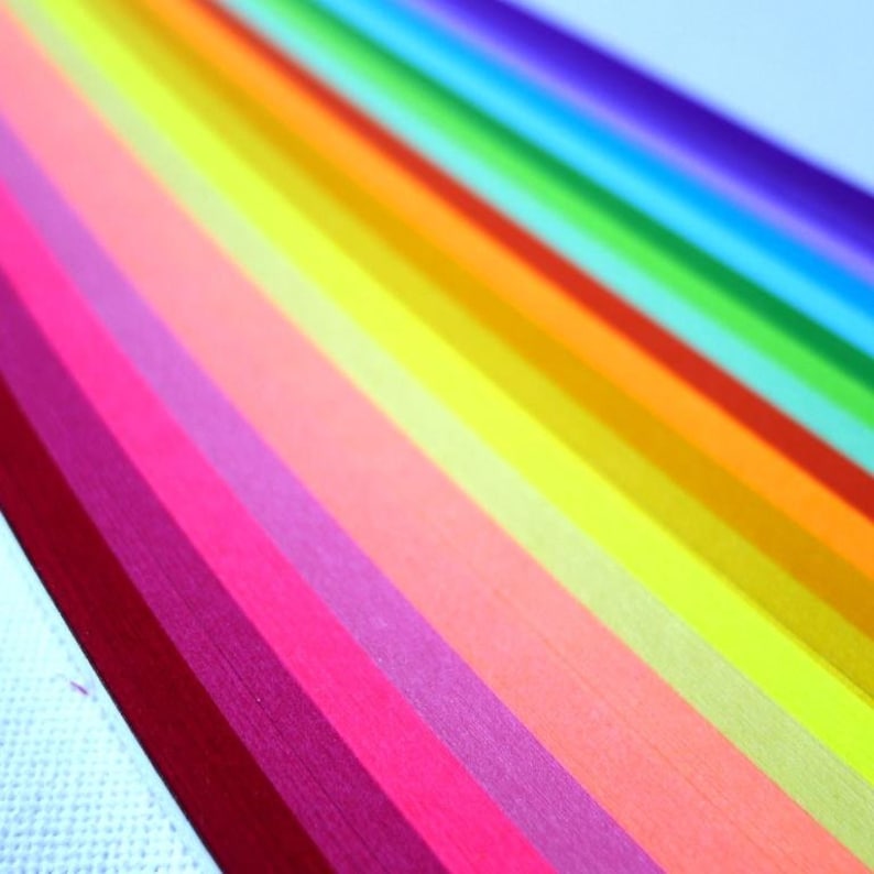 May include: A rainbow of colorful paper strips, arranged in a fan shape, with the colors ranging from deep red to light purple.