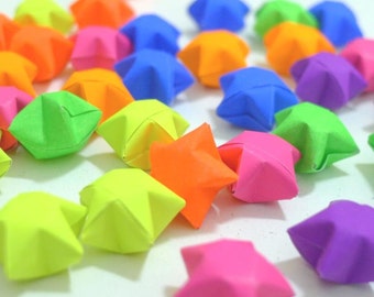 May include: A collection of colorful origami stars in various shades of green, blue, pink, orange, purple, and yellow. The stars are made of paper and are folded into a five-pointed star shape.