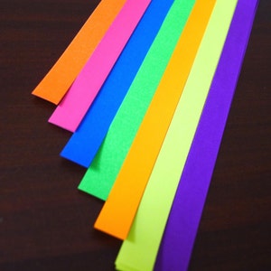 K&ouml;nnte beinhalten: Sieben Streifen farbiges Papier, die in einem Regenbogenmuster angeordnet sind, mit den Farben Orange, Rosa, Blau, Gr&uuml;n, Gelb und Lila.