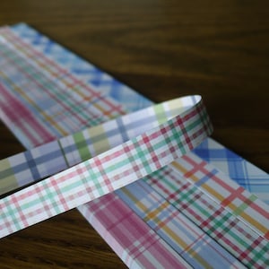 May include: A close-up of a stack of colourful plaid ribbon. The ribbon is folded and has a checkered pattern in shades of pink, blue, green, and yellow.
