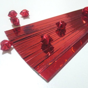 May include: Red origami paper strips for making stars. The strips are arranged in a fan shape with several finished red origami stars scattered around.