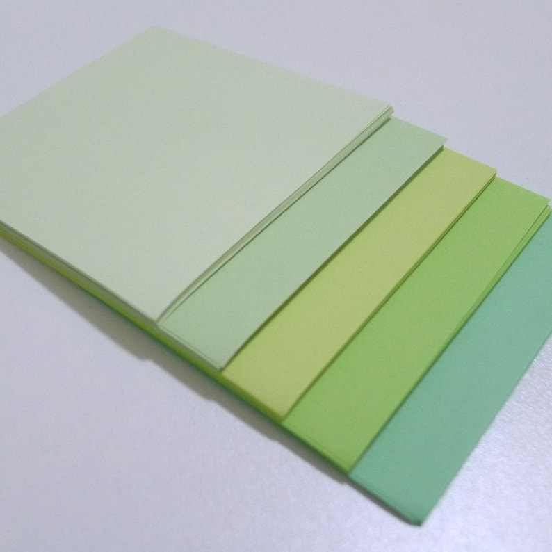 May include: Stack of five sheets of paper in various shades of green, from light green to dark green.