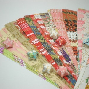 May include: A collection of colorful origami paper strips in various patterns, including floral, geometric, and traditional Japanese designs. The paper is arranged in a fan shape, with several folded origami stars scattered around the paper.