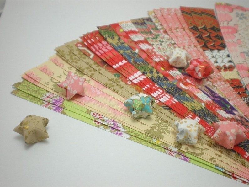 May include: A collection of colorful origami paper strips with a variety of floral and geometric patterns. Several origami stars made from the paper are scattered around the strips.