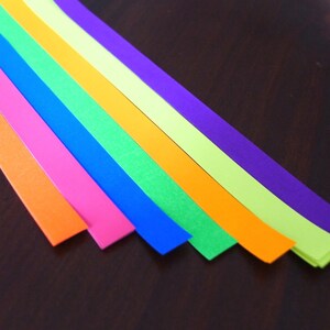 K&ouml;nnte beinhalten: Sieben Streifen aus farbigem Papier, die in einem Regenbogenmuster angeordnet sind, mit den Farben Rot, Orange, Gelb, Gr&uuml;n, Blau, Indigo und Violett.