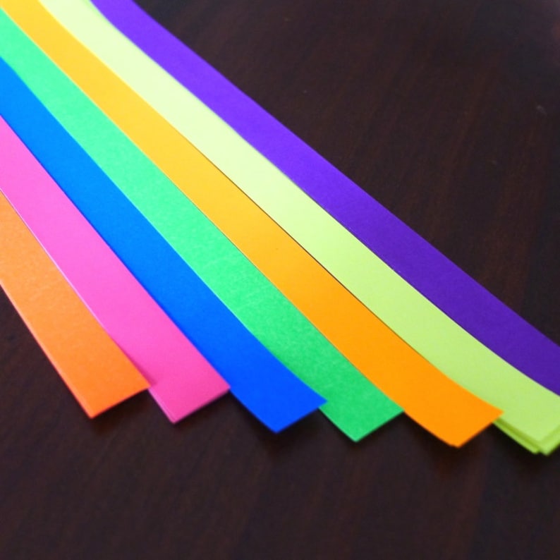 K&ouml;nnte beinhalten: Sieben Streifen aus farbigem Papier, die in einem Regenbogenmuster angeordnet sind, mit den Farben Rot, Orange, Gelb, Gr&uuml;n, Blau, Indigo und Violett.