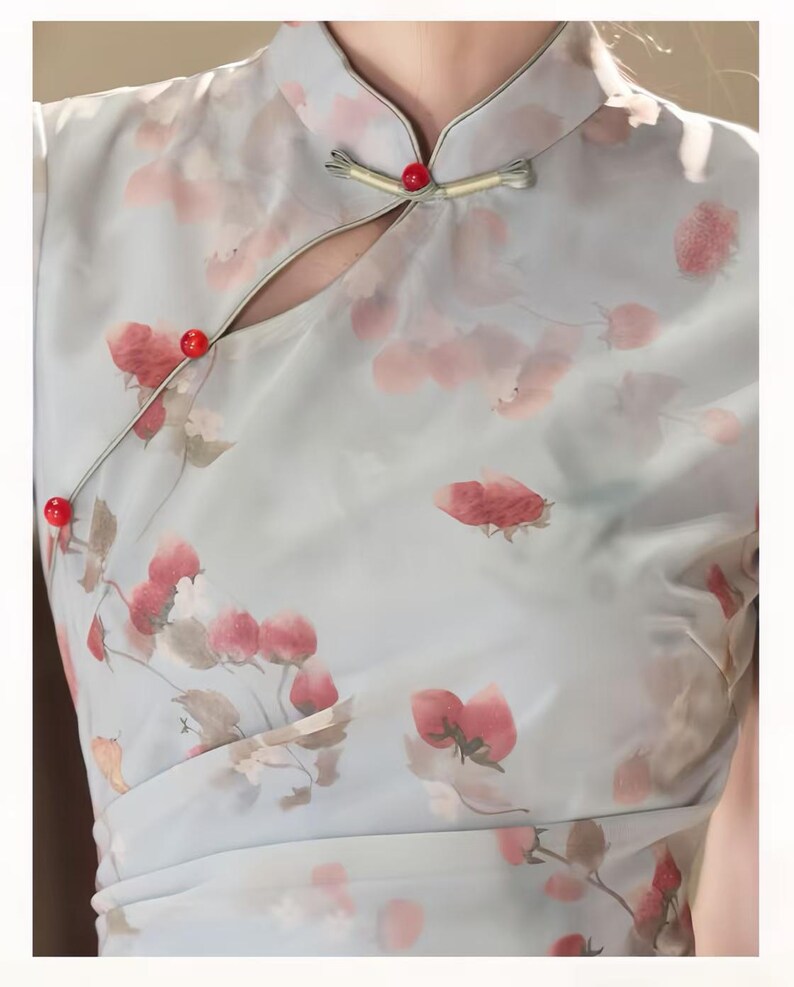 May include: A light blue dress featuring a strawberry print in shades of red and pink. The garment has a mandarin collar, a side-fastening closure with three small red spherical buttons, and a diagonal overlapping front panel design.