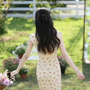 May include: A cream-colored midi dress featuring a repeating pattern of small orange and red floral motifs. The garment has short cap sleeves, a fitted bodice, and a straight silhouette that extends to the mid-calf, viewed from the back.