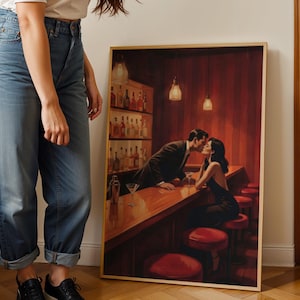 May include: A framed print depicts a couple kissing at a bar. The bar has a wooden counter, red stools, and a shelf of liquor bottles. The artwork is in a warm color palette with red and brown tones.