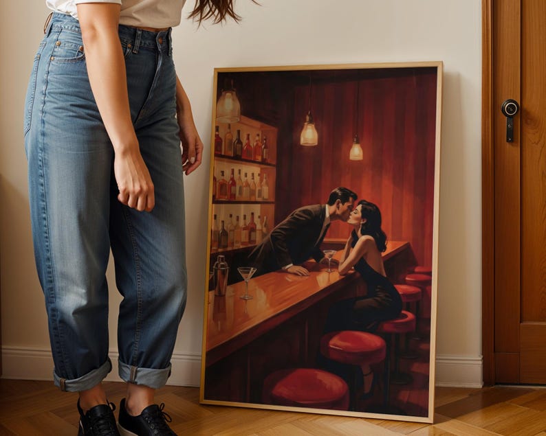 May include: A framed print depicts a couple kissing at a bar. The bar has a wooden counter, red stools, and a shelf of liquor bottles. The artwork is in a warm color palette with red and brown tones.