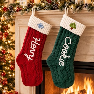 May include: Two cable-knit Christmas stockings, one red and one green, featuring white ribbed cuffs. The red stocking is embroidered with the name Henry and a blue snowflake, while the green stocking features the name Cookie and a small tree.