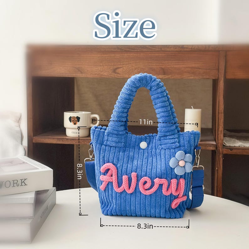May include: Blue corduroy tote bag with the name "Avery" in pink script. The bag has a flower accent and a shoulder strap. It measures 11 inches wide and 8.3 inches high.
