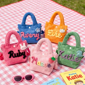 Peut inclure: Cinq sacs fourre-tout en velours côtelé colorés avec des noms brodés. Les sacs sont dans les tons de bleu, orange, rose, rose clair et vert. Chaque sac a une poignée assortie et un petit charme décoratif. Des lunettes de soleil roses et deux livres sont au premier plan.
