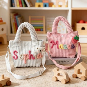 May include: Two corduroy tote bags, one in white and one in pink, with embroidered names. The white bag has "Sophia" in pink and cream letters, and a teddy bear charm. The pink bag features "Maeve" in colourful letters and a strawberry applique. Both have shoulder straps.