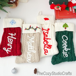 May include: A selection of cable-knit Christmas stockings in red, beige, white, and green. Each stocking has a white cuff and a name embroidered in a contrasting colour. Festive details include a snowflake, fairy lights, a Santa hat, and a Christmas tree.