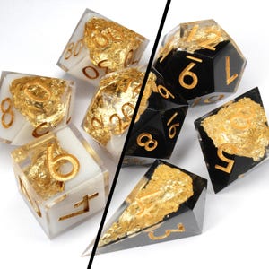 May include: A set of black and white dice with gold leaf accents. The dice are made of resin and have a clear finish. The dice are numbered 1-6 and 8. The dice are ideal for role-playing games.