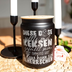 Pode incluir: Um pote de biscoitos preto com tampa de madeira e o texto "Diese Dose sollte mit Keksen gefüllt sein, aber niemand hier im Haus kann sich beherrschen" gravado no lado.