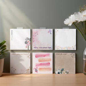 Puede incluir: Seis diseños diferentes de blocs de notas en blanco con diseños florales y abstractos en acuarela. Los blocs de notas son todos cuadrados y tienen un fondo blanco. El texto en los blocs de notas incluye "Mama - mein schцnstes Mam", "Alles beginnt mit Mama", "Mama for ever" y "Mama".