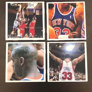 May include: Four square ceramic coasters featuring images of basketball players. The first coaster shows two players in red and white uniforms jumping for a basketball. The second coaster shows a player in a blue and white uniform with the text "NEW YORK 32". The third coaster shows a close-up of a player's head with a shaved design. The fourth coaster shows a player in a white and red uniform with the text "EWING 33" and arms outstretched.