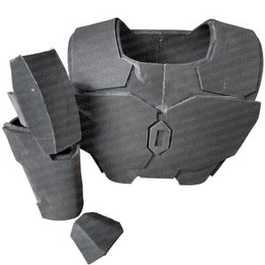Puede incluir: Un conjunto de armadura de espuma gris oscuro, probablemente para cosplay o disfraces. La armadura segmentada incluye una pieza para el pecho, hombreras y protectores de brazos. Las piezas están separadas y sin pintar, con formas geométricas.