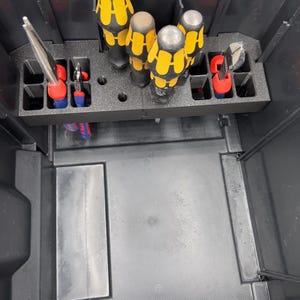 Könnte beinhalten: Eine schwarze Werkzeugkiste mit verschiedenen Werkzeugen. Die Werkzeuge umfassen Schraubendreher mit gelben und schwarzen Griffen sowie Werkzeuge mit roten und blauen Griffen. Die Werkzeugkiste hat einen integrierten Organizer, um die Werkzeuge zu halten.