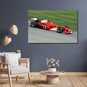 May include: A framed canvas print of a red Formula 1 race car speeding on a track. The car has white accents and sponsor logos. The background shows a green grassy area and a gray track.