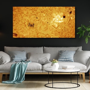May include: A large, rectangular canvas print depicting a close-up view of the sun's surface, with swirling patterns and dark spots. A small, detailed image of the International Space Station is visible. The print is displayed above a gray sofa with blue and white striped pillows.