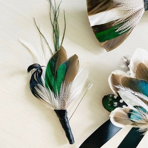 May include: Two feather buttonholes with a black ribbon. One buttonhole is green, brown, and white. The other buttonhole is brown, white, and teal. Both buttonholes have a black pin.