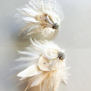 Op de afbeelding: Twee cr&egrave;mekleurige haaraccessoires van veren met delicaat wit net, gelaagde pluimen en een zilverkleurige versiering in het midden met kleine heldere kristallen. De tekst {kirahley kreations} is zichtbaar bovenaan de afbeelding.
