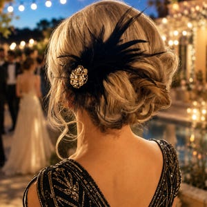 May include: A hair accessory featuring black feathers and a circular gold-toned brooch with clear crystals, worn in a blonde updo. The garment is a black sleeveless dress with gold geometric embroidery and the text kirahley kreations.