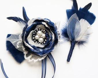 Puede incluir: Un ramillete de flores de tela azul marino y blanco con un centro de perlas y pedrería, acompañado de un prendido a juego con plumas, hojas esqueleto y un alfiler con punta de perla, con el texto {kirahley kreations}.