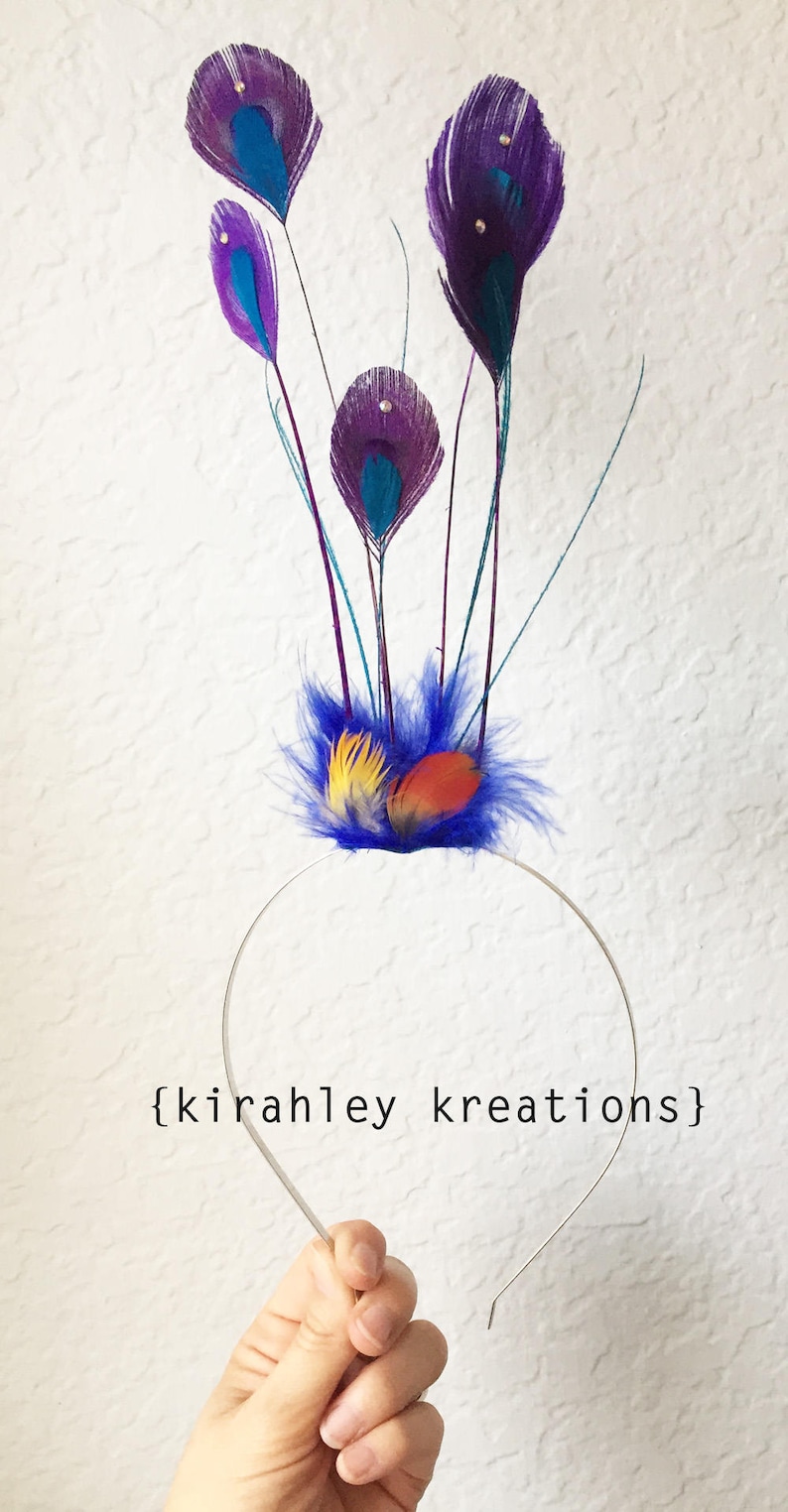 May include: A handmade headband featuring peacock feather accents. The headpiece has a silver band with a cluster of purple, teal, yellow, and orange feathers. The text "{kirahley kreations}" is printed on the image.