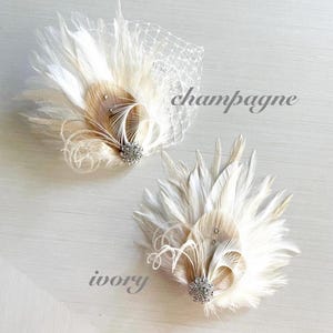 Op de afbeelding: Twee decoratieve haaraccessoires met witte en champagnekleurige veren, een centrale kristallen versiering en gekrulde accenten. E&eacute;n stuk bevat een witte netsluier. De tekst champagne, ivory en {kirahley kreations} is zichtbaar.