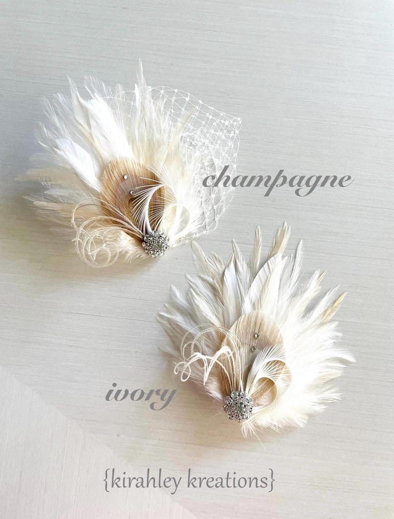 Op de afbeelding: Twee decoratieve haaraccessoires met witte en champagnekleurige veren, een centrale kristallen versiering en gekrulde accenten. E&eacute;n stuk bevat een witte netsluier. De tekst champagne, ivory en {kirahley kreations} is zichtbaar.