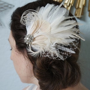 May include: A white and beige feather hair comb with a crystal embellishment. The comb is worn in a woman's hair.