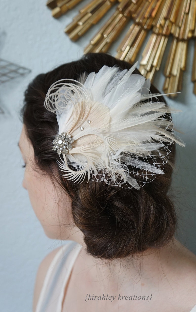 May include: A white and beige feather hair comb with a crystal embellishment. The comb is worn in a woman's hair.